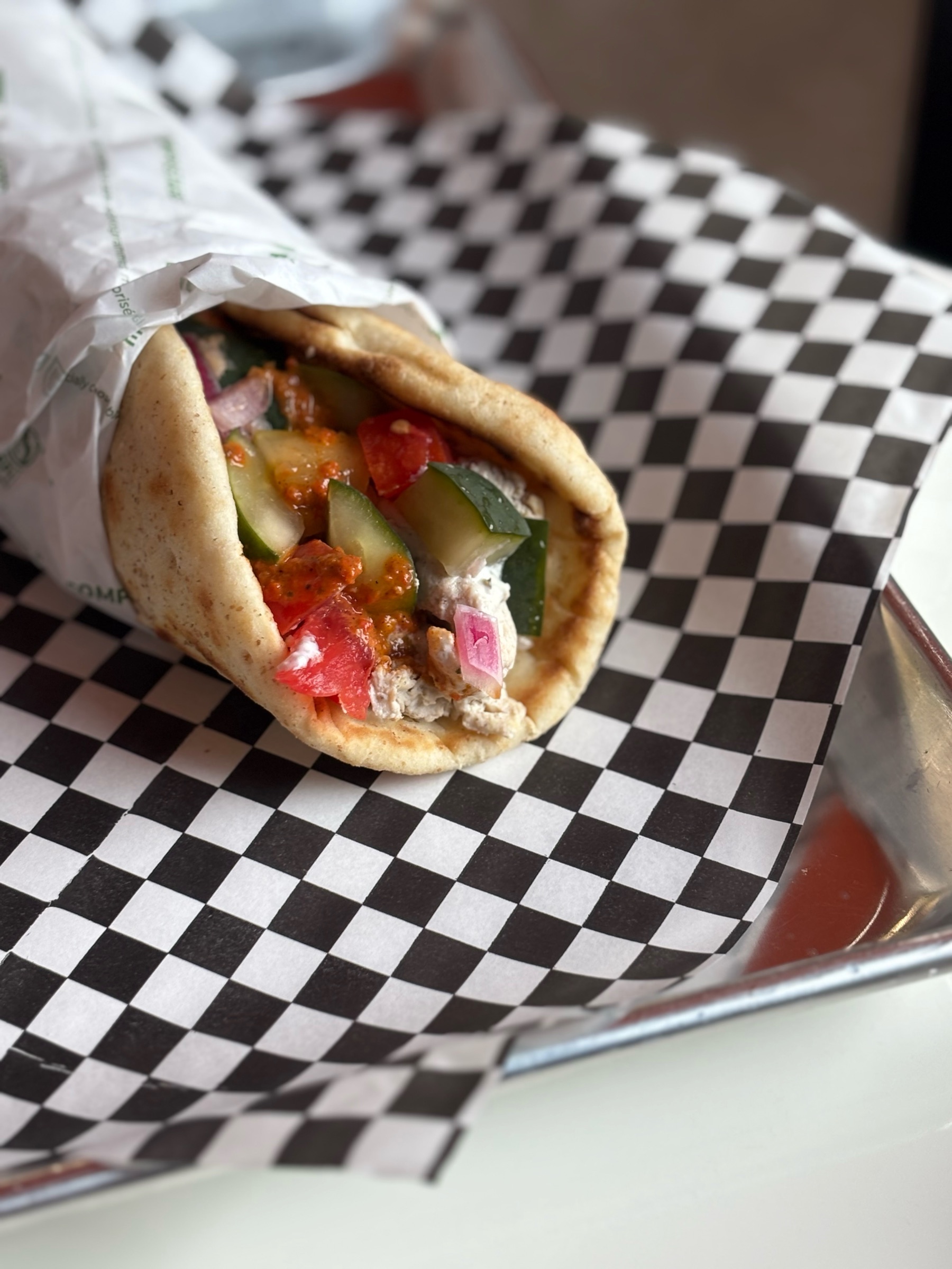 A shawarma in a pita, wrapped in paper on checkered paper